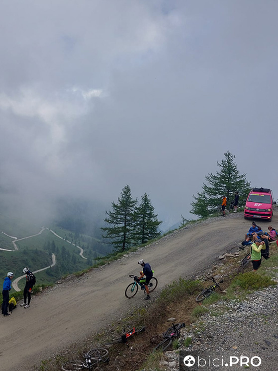Quasi in vetta arriva la foschia, si accumulano tifosi in bici e mezzi dei team mentre si sta decidendo l'accorciamento della tappa
